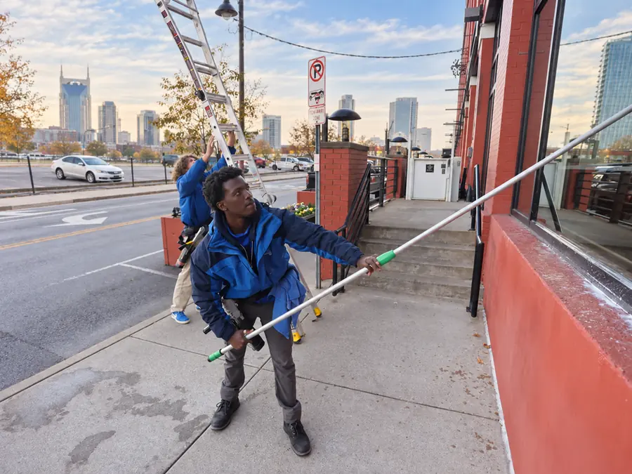 A Camelot window cleaner using a water-fed pole on a downtown Nashville storefront